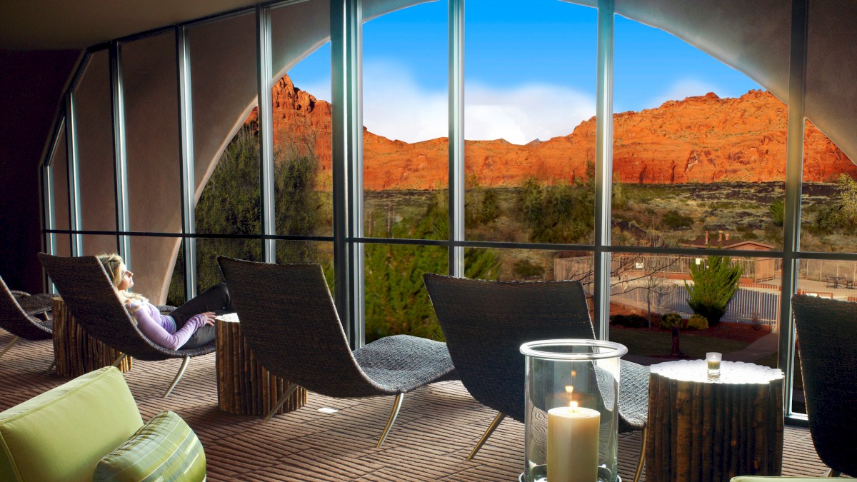 A serene lounge with modern seating and large windows offers a stunning view of red rock formations, featuring a calm person resting.