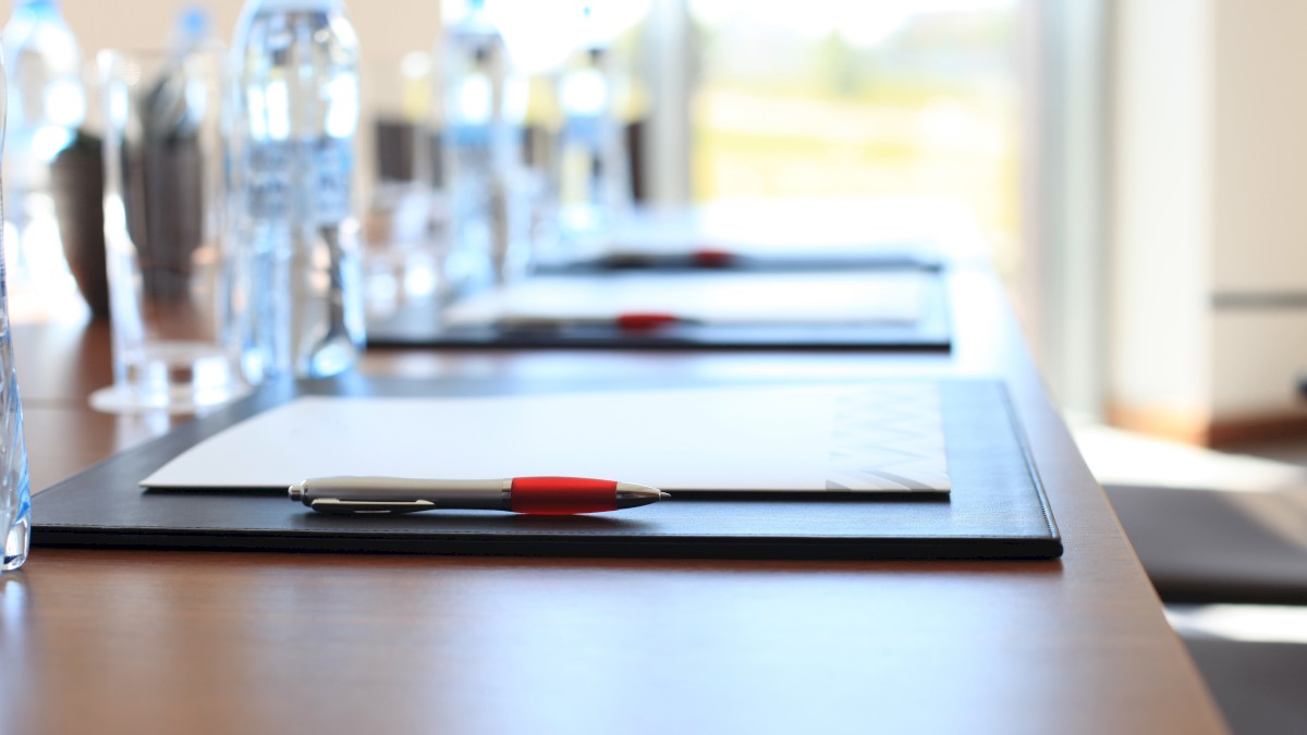 A conference table set with notepads, pens, and bottled water is shown in the image.