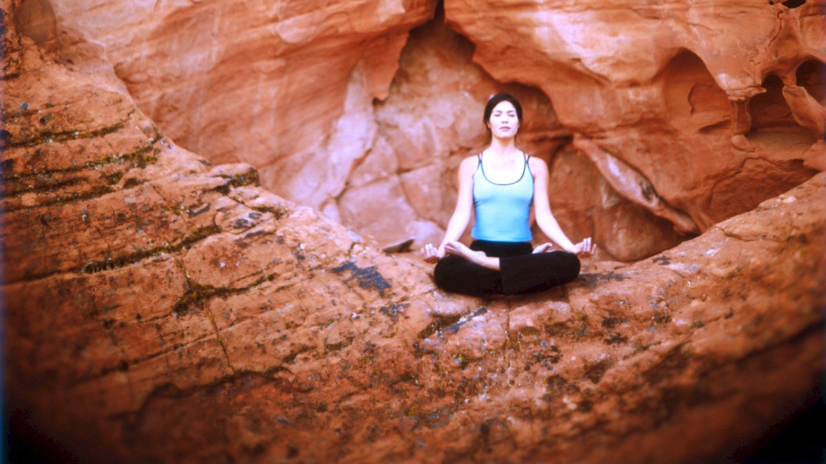 A person sits in a meditative pose against a backdrop of red rock formations.