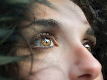 The image features a close-up of a person's face, focusing on their expressive eyes and a portion of their nose, surrounded by dark hair.