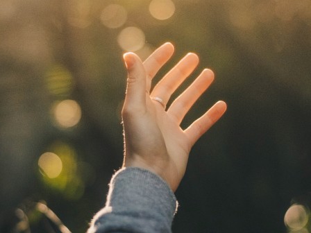 A hand reaching out toward the sunlight in a blurred outdoor background, surrounded by a soft bokeh effect.