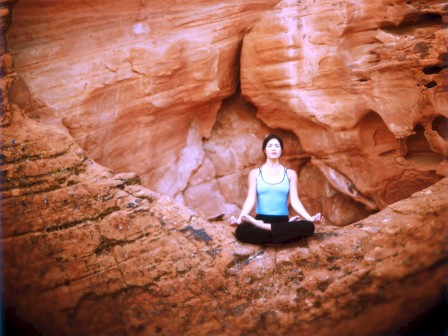 A person sits in a meditative pose against a backdrop of beautiful red rock formations, blending harmoniously with the natural surroundings.