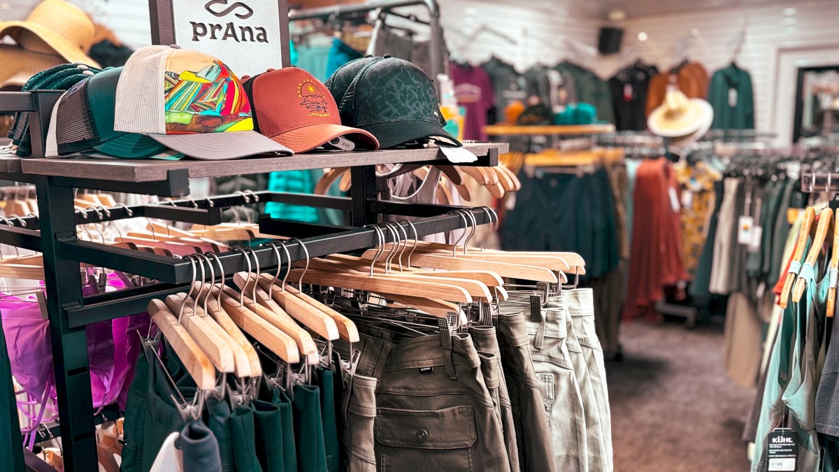 A clothing store with various apparel, including shorts, hats, and shirts, displayed on racks, featuring a Prana brand sign.