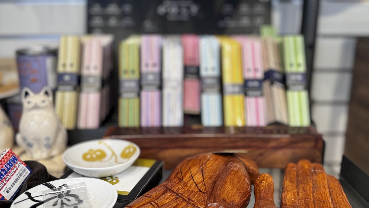 The image shows a display shelf with various items including incense sticks, wooden hand sculptures, a ceramic cat figurine, and decorative plates.