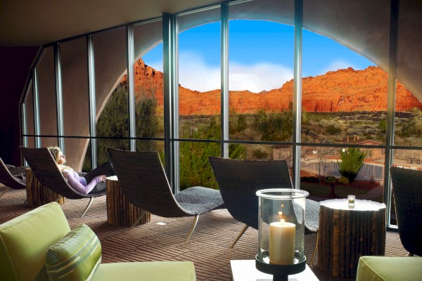 A modern lounge area with large windows overlooks a scenic desert landscape, featuring comfortable seating and a candle on a table.