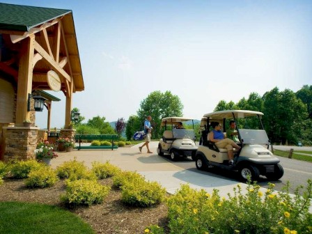 The image depicts a golf course scene with two golf carts and people either in or around them, next to a building and surrounded by greenery.