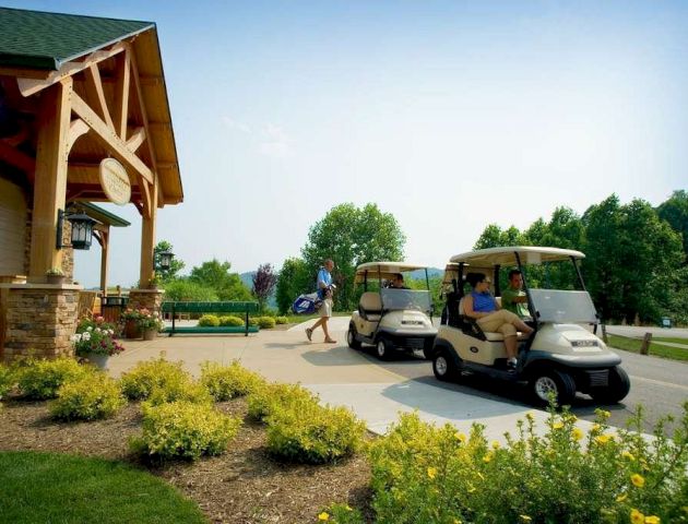 The image shows a golf course scene with people in golf carts and a person carrying golf clubs near a building with landscaped plants and flowers.